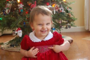 toddler smiling in a christmas dress in front of a christmas tree