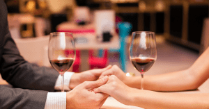 a couples hands clasped over two glasses of wine on a date