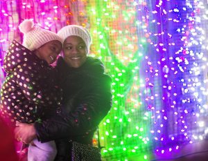 A mother and child are looking at brightly colored lights at the yearly Zoolights display at stone zoo