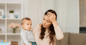 mother holding her baby with hand on head looking stressed.