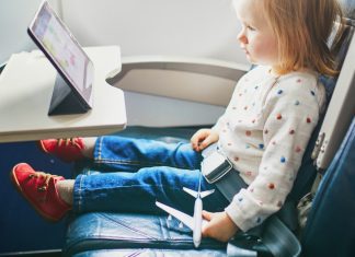 toddler sitting on an airplane watching an ipad and holding a toy airplane - tips for going on vacation with a toddler